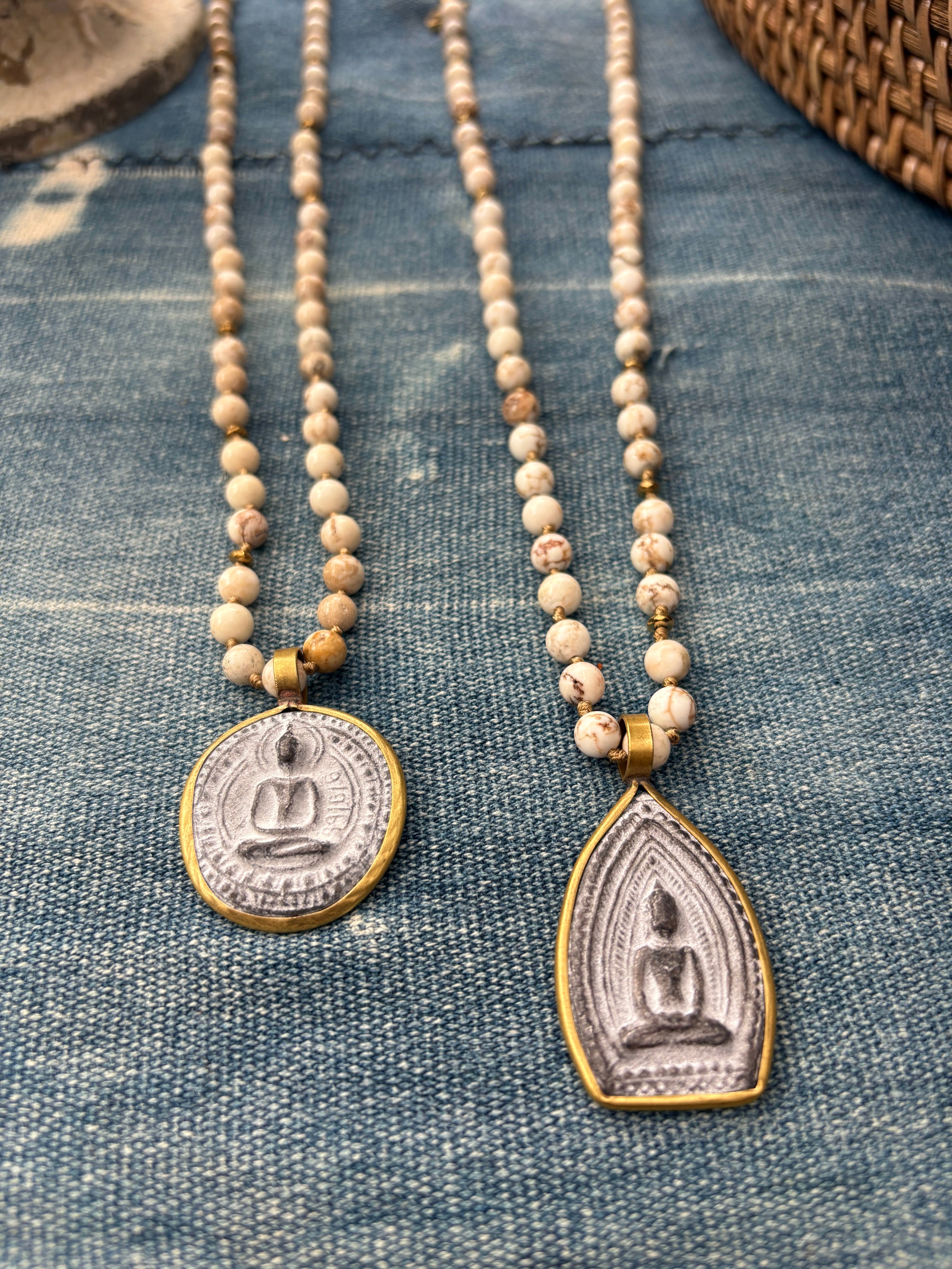 Two beaded necklaces with Buddha pendants on a denim surface