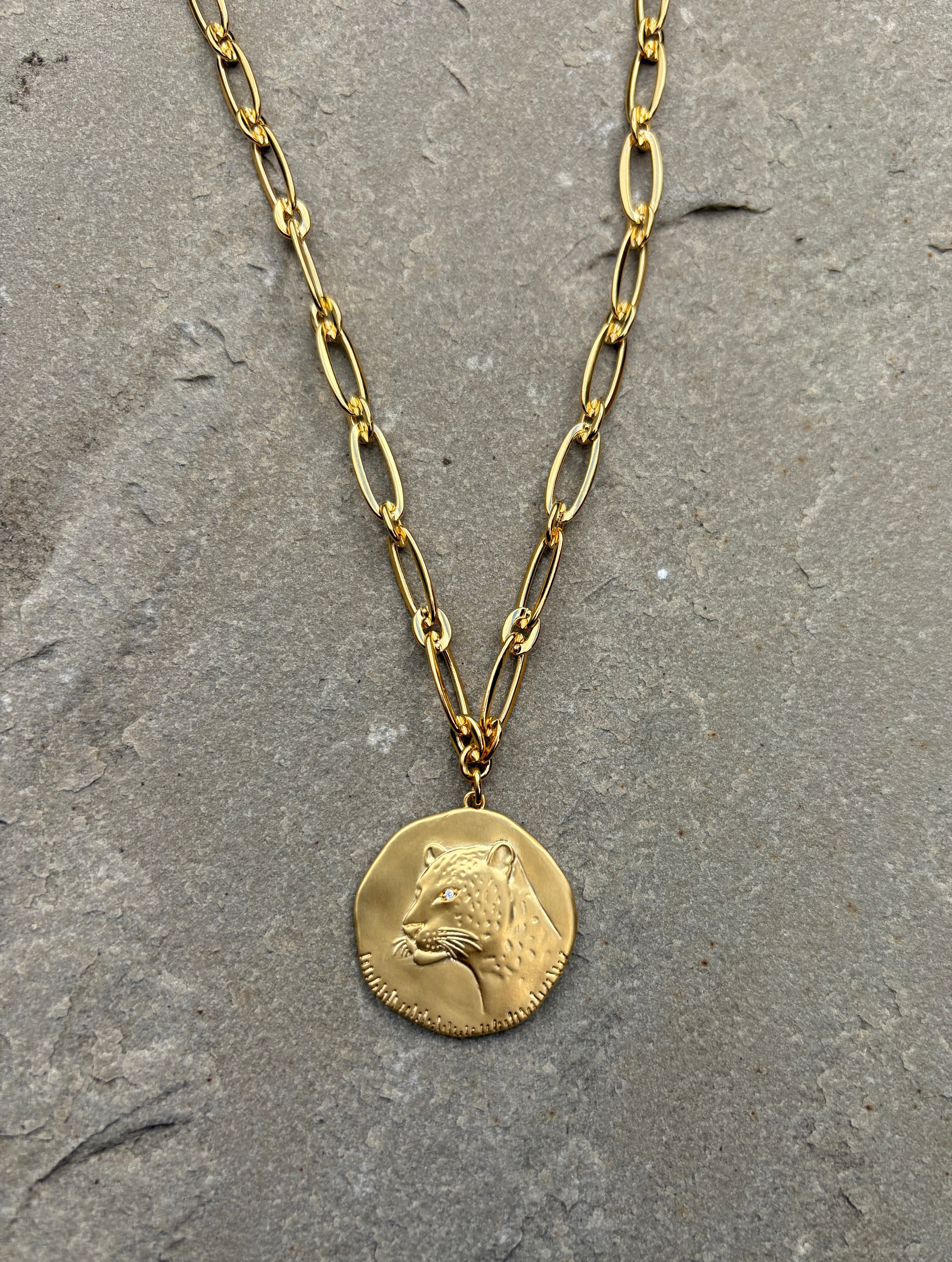 Gold necklace with a bear head pendant on a gray stone surface