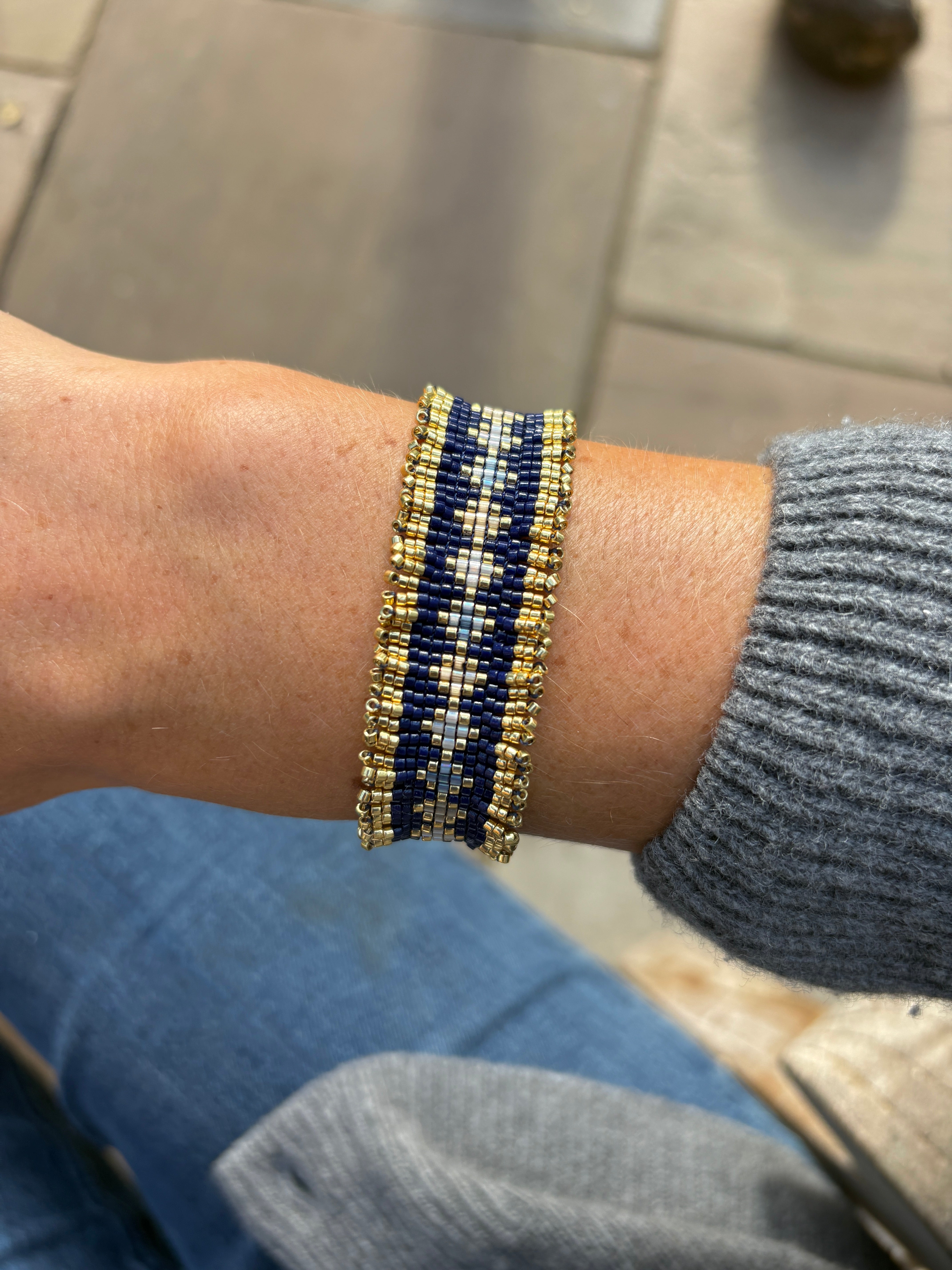 Close-up of a wrist wearing a blue and gold beaded bracelet on a neutral background.