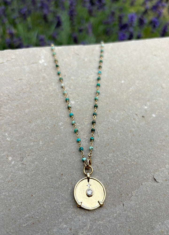 Necklace with a round pendant on a stone surface with lavender in the background