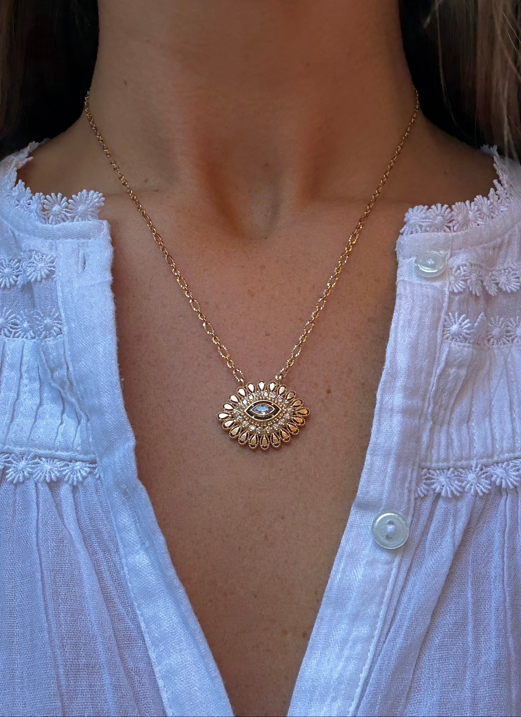 Gold necklace with a sunflower pendant worn by a person in a white blouse.