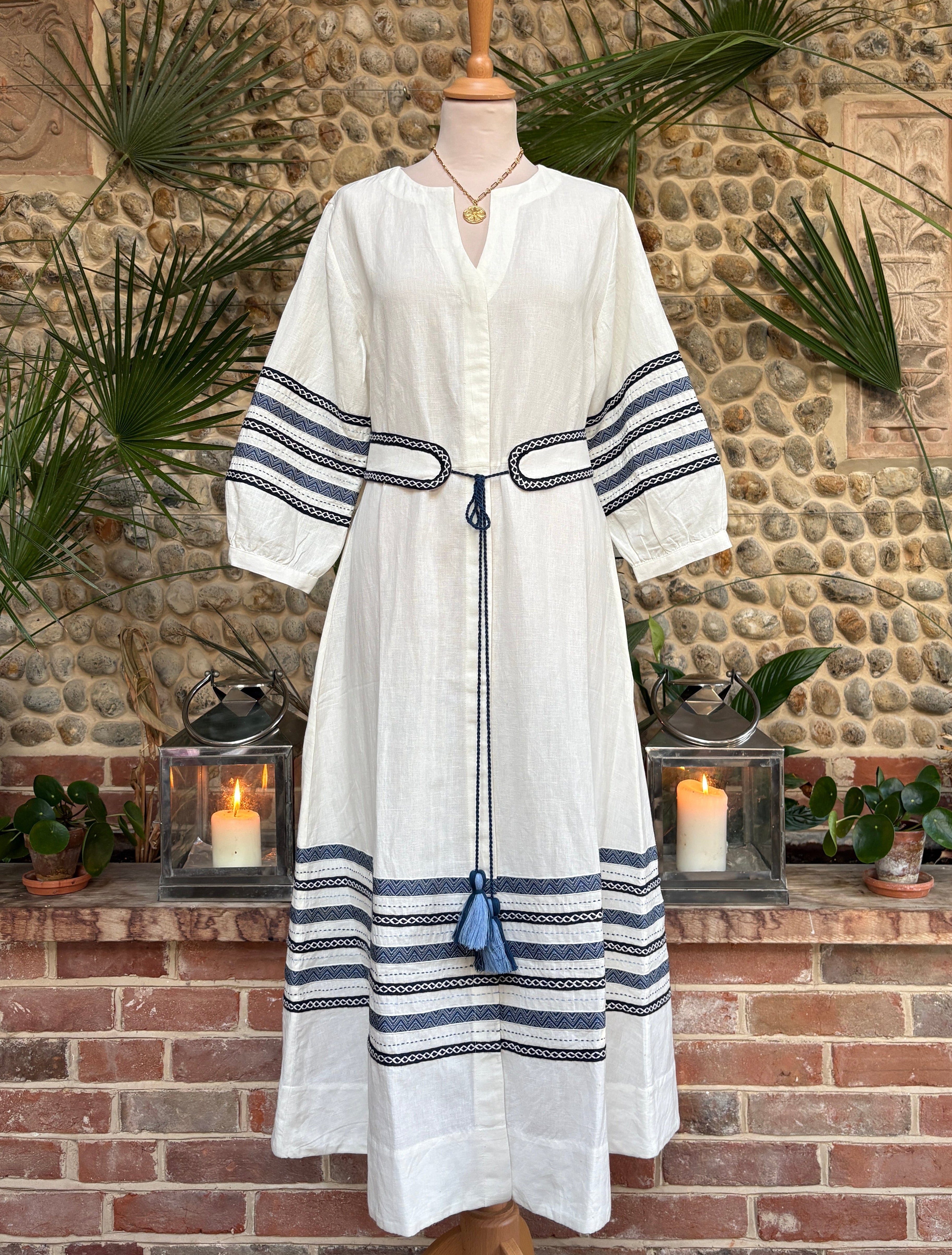 White robe with blue stripes on a mannequin against a stone wall background