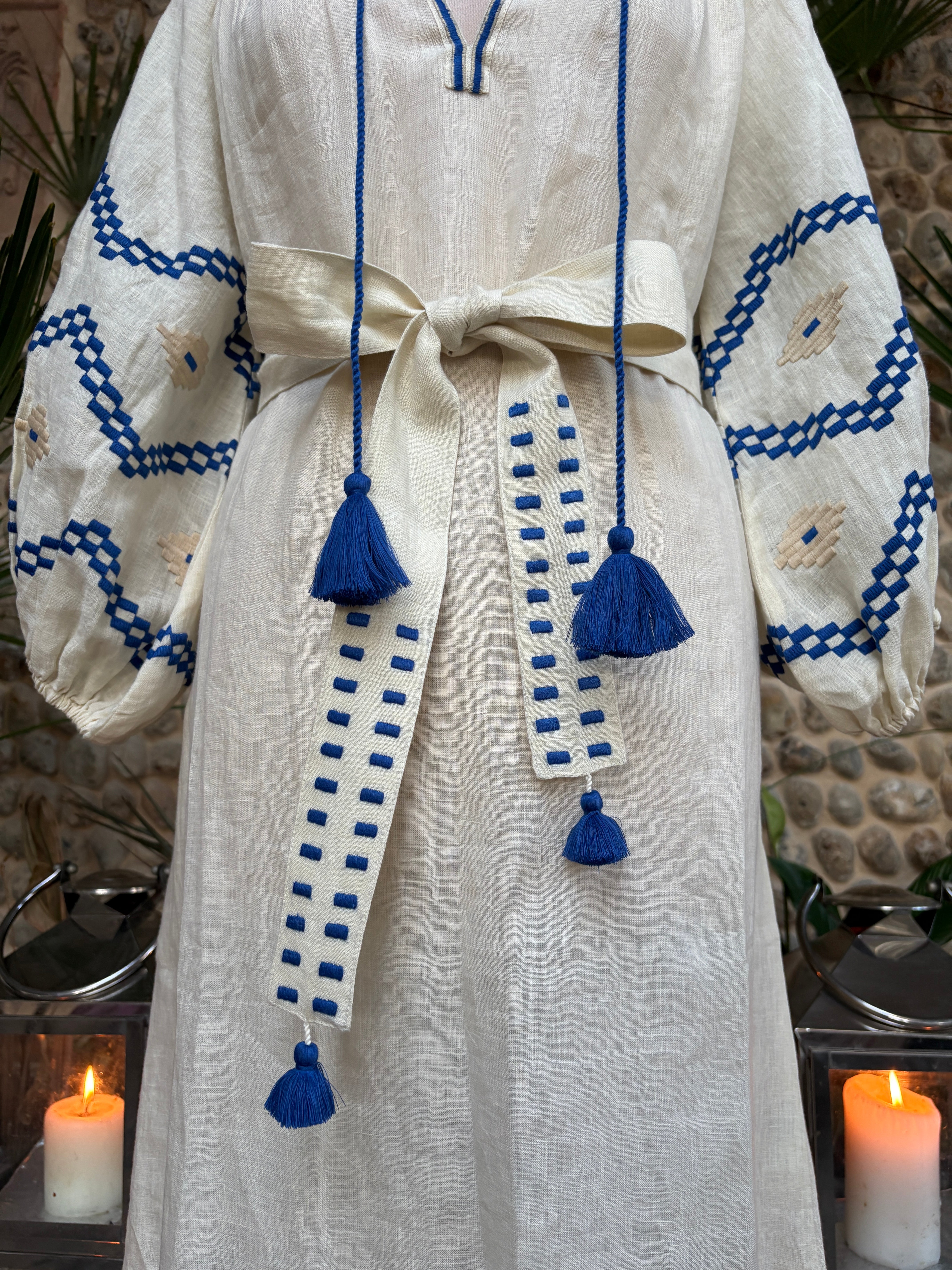 White garment with blue embroidery and tassels on a textured surface. benaras by citrus