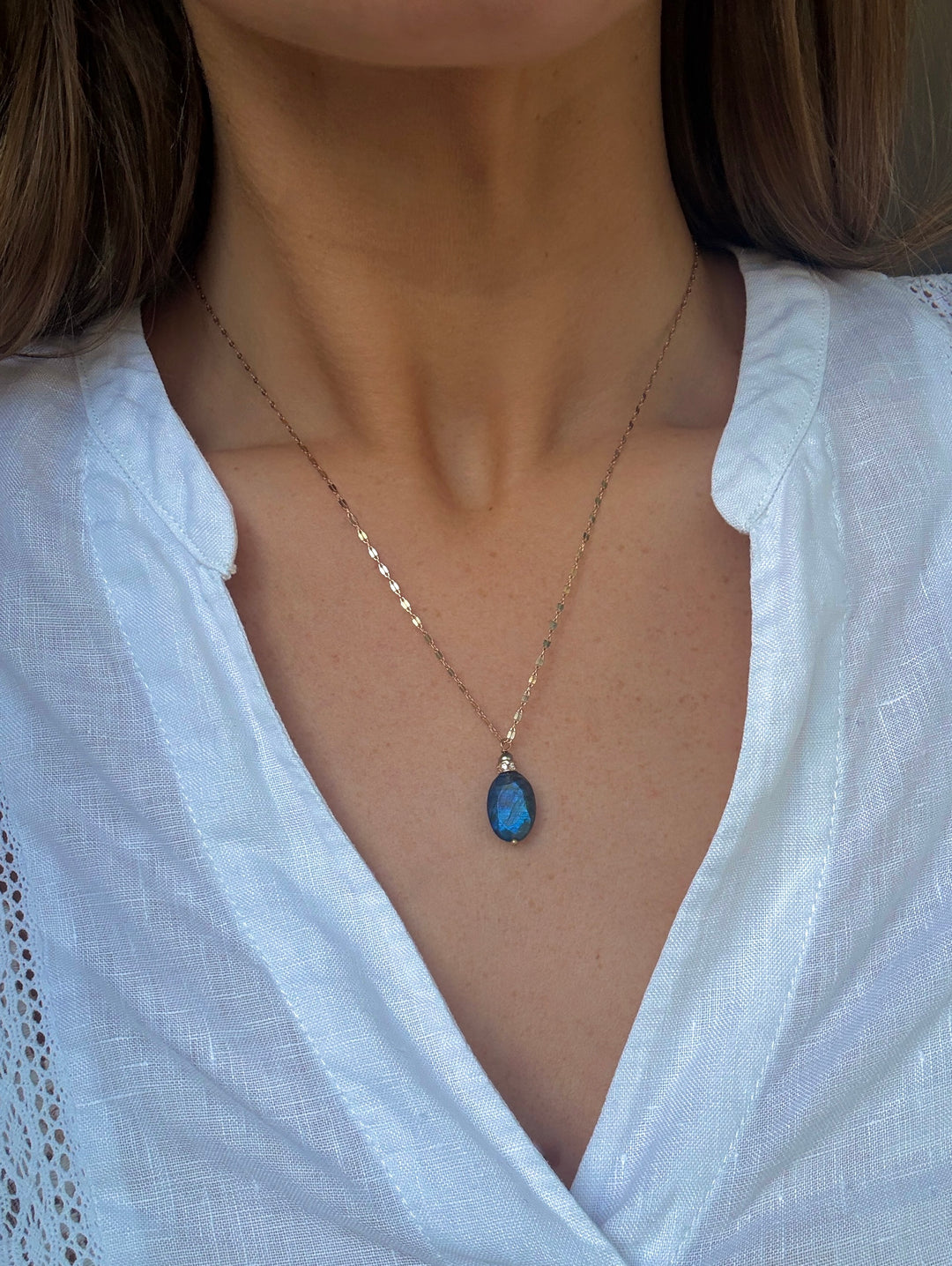 Necklace with a blue pendant worn by a person in a white shirt