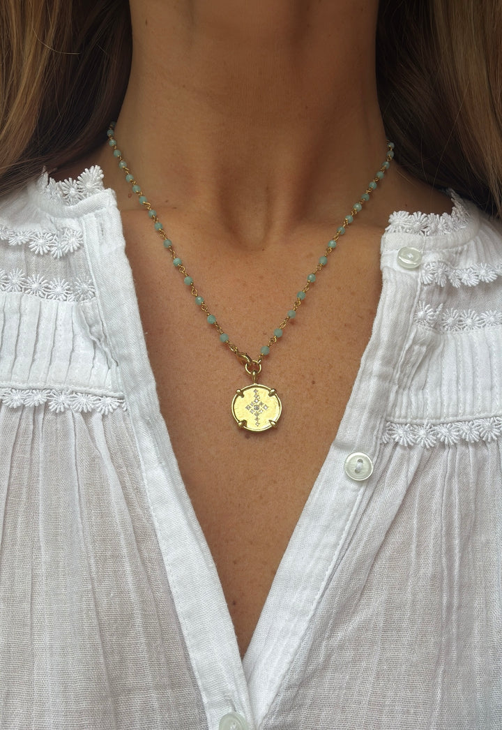 Necklace with a gold pendant worn by a person in a white blouse