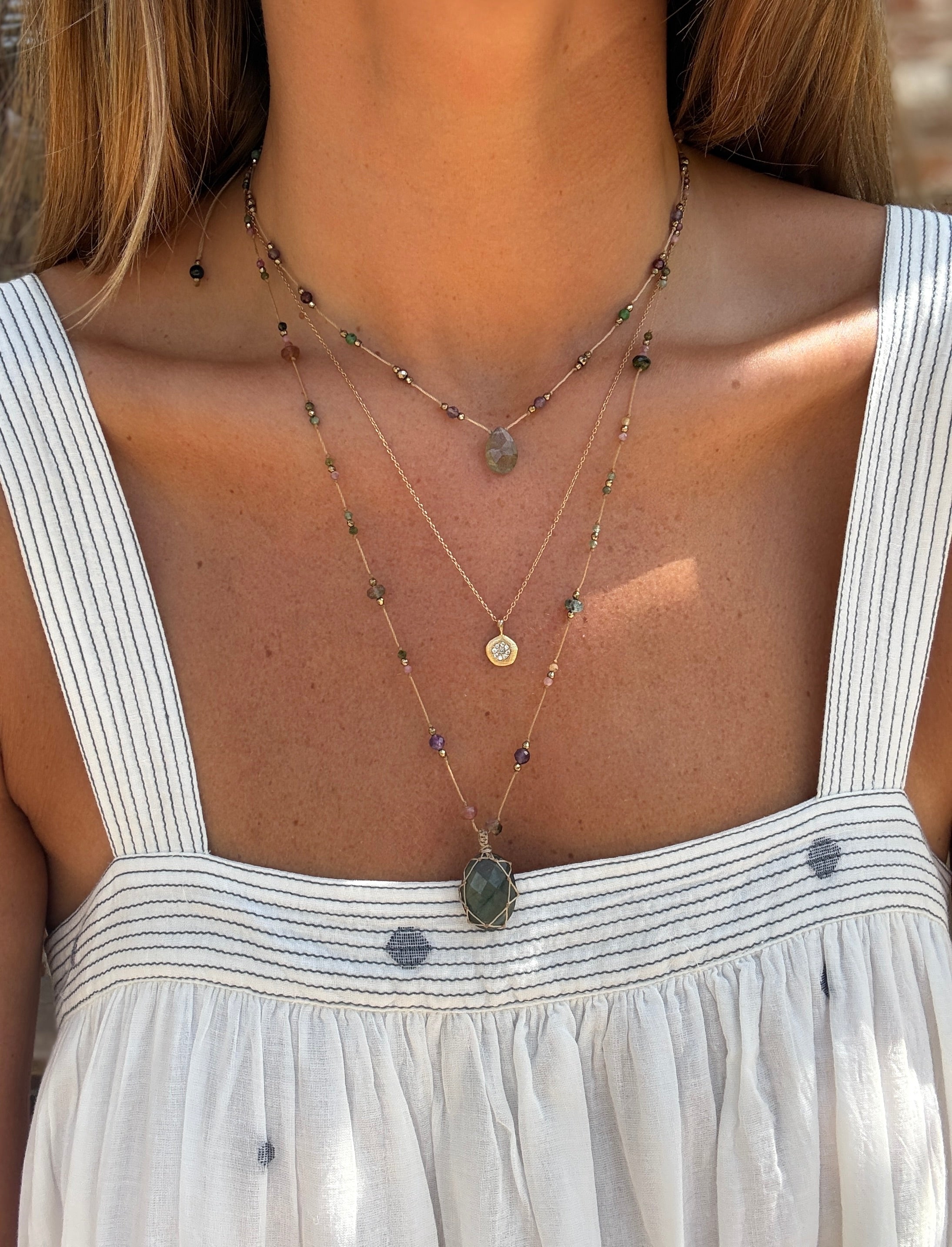 Close-up of a person wearing layered necklaces with a white dress.