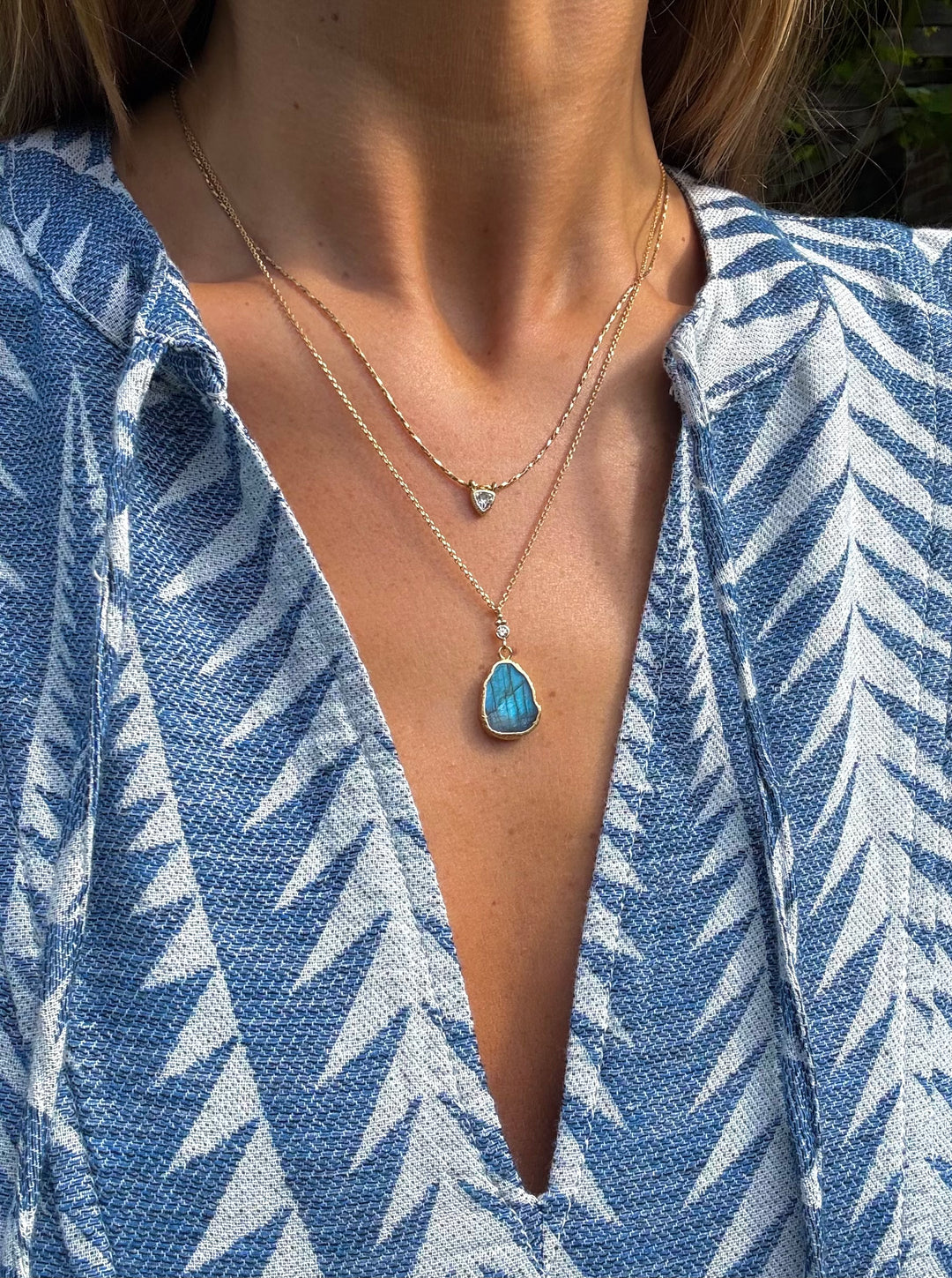 Person wearing a blue patterned garment with a necklace featuring a blue pendant.