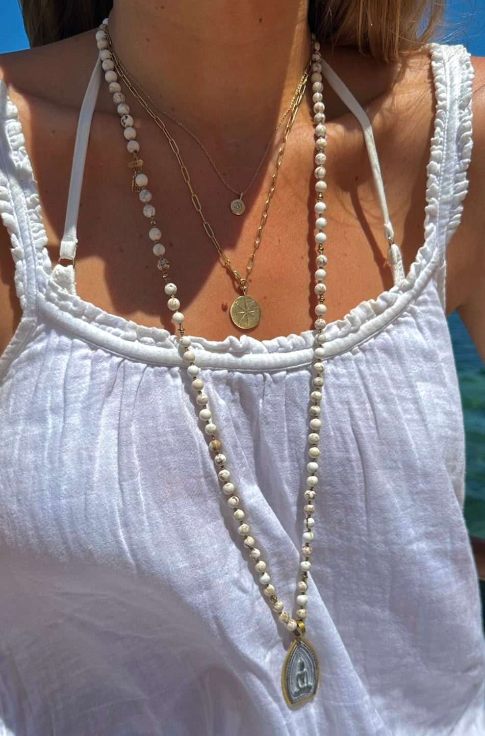 Person wearing a white dress with layered necklaces against a blue background