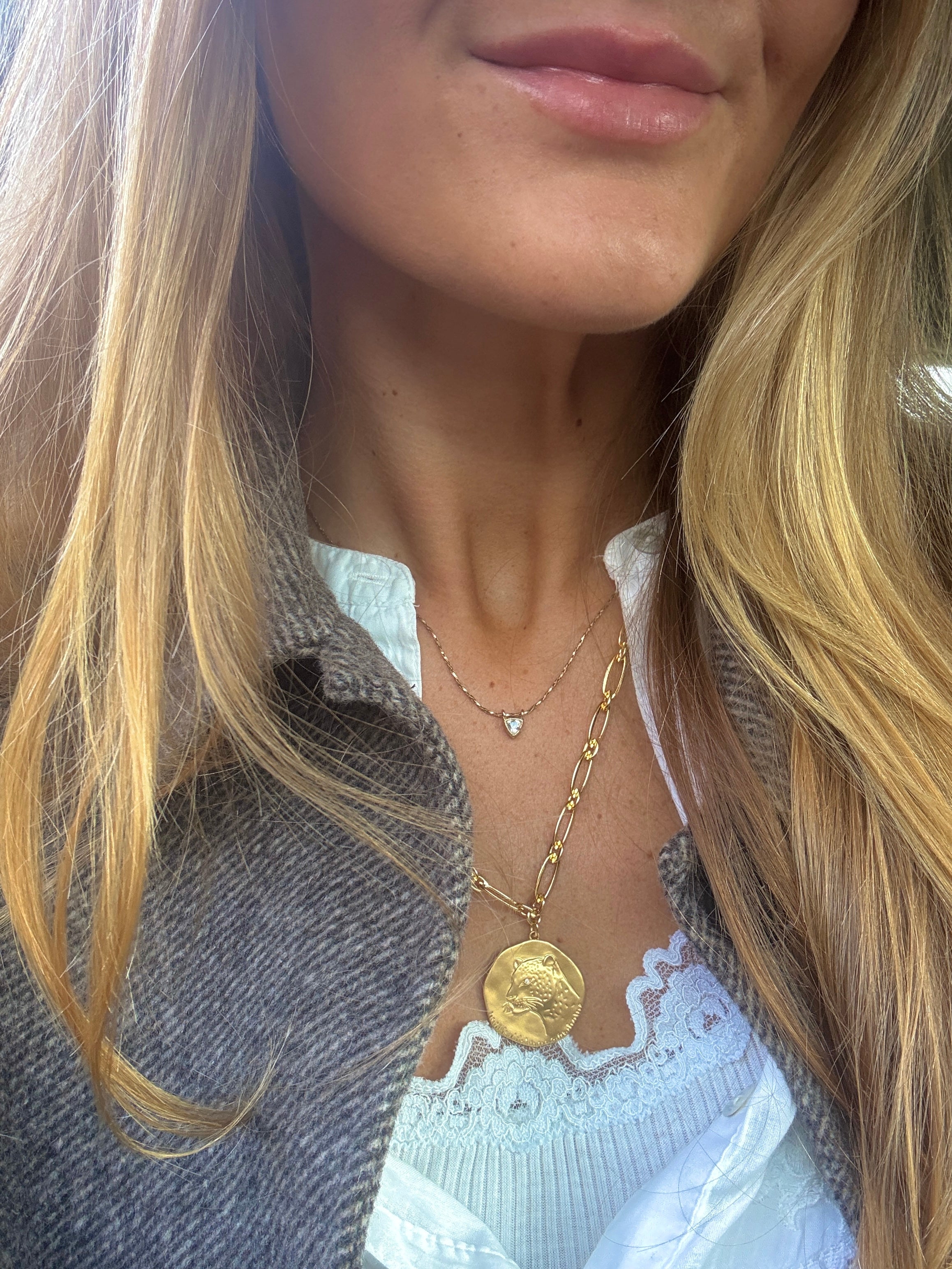 Close-up of a person wearing a gold necklace with a coin pendant.