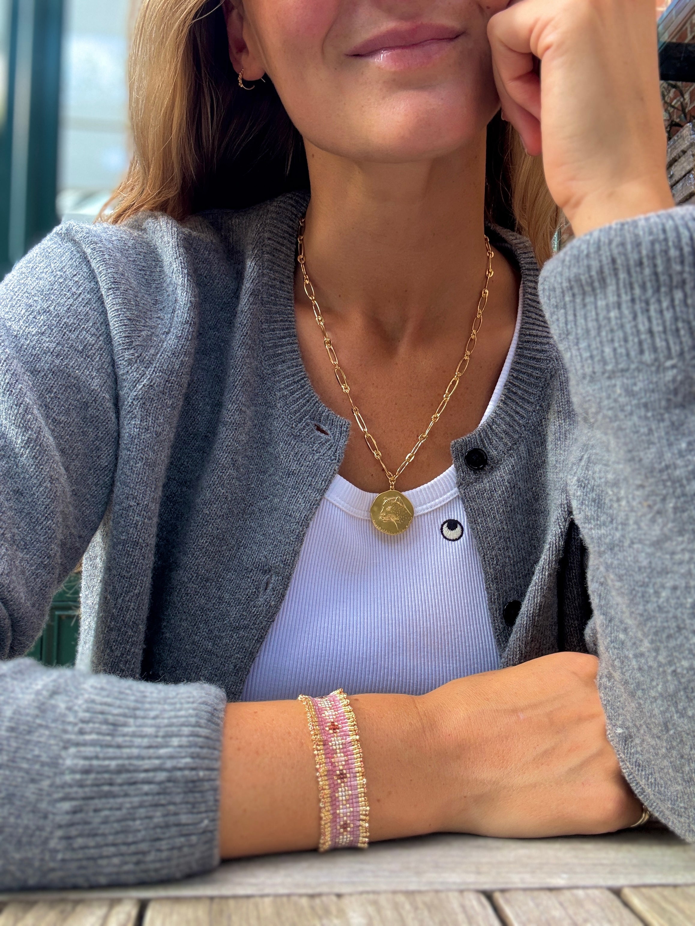 Woman wearing a gold necklace and bracelet on a wooden surface