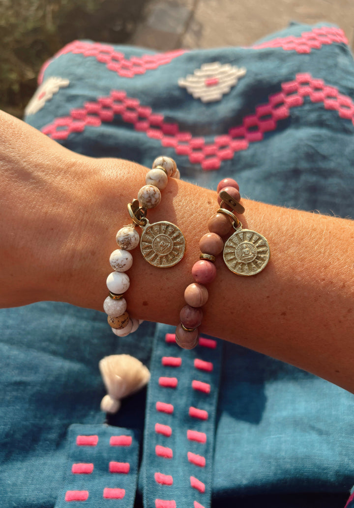 Two beaded bracelets with gold coin charms worn on a person&