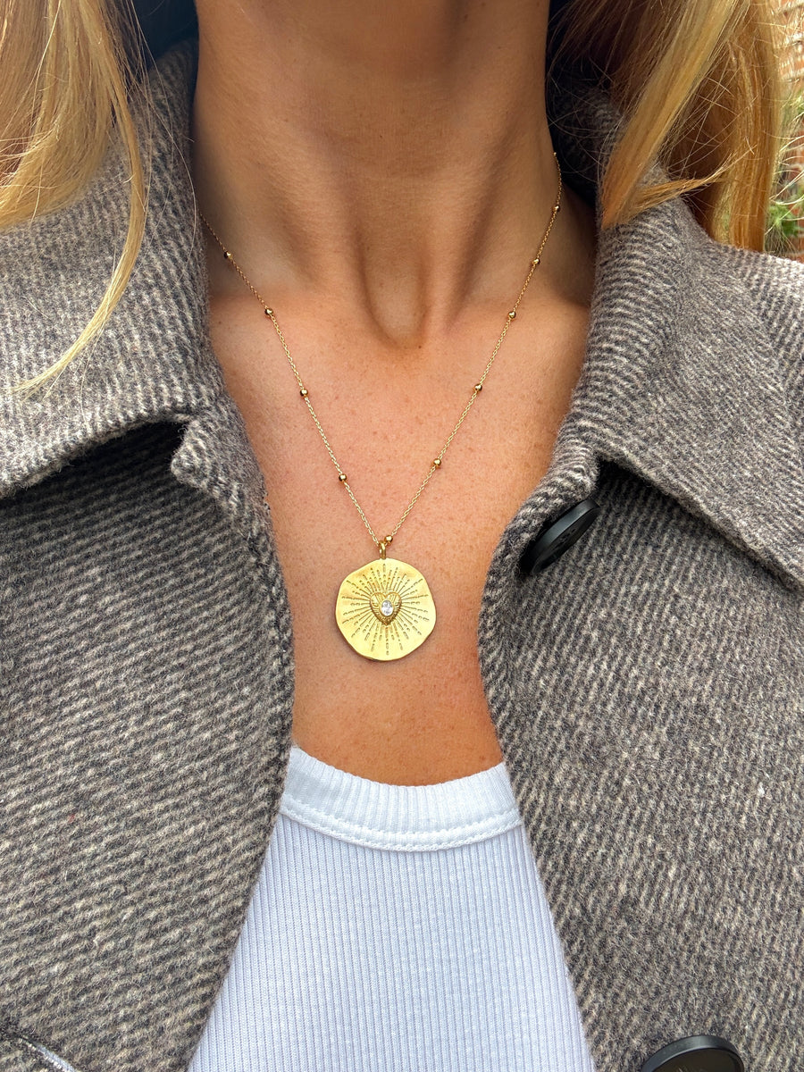 Gold necklace with a circular pendant worn by a person in a gray coat.