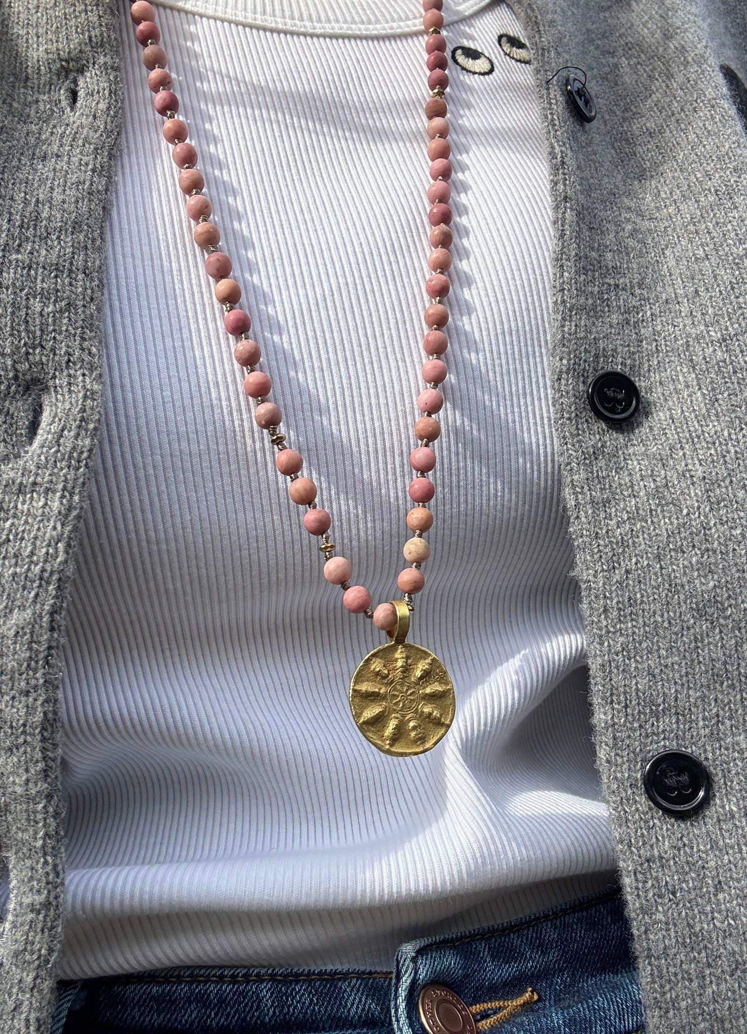 Necklace with pink beads and a gold pendant on a white shirt and gray cardigan.